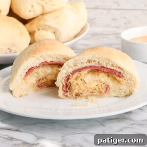 Reuben Stromboli sliced in half to show corned beef, swiss, and sauerkraut inside. Additional Reuben Rolls are in the background.