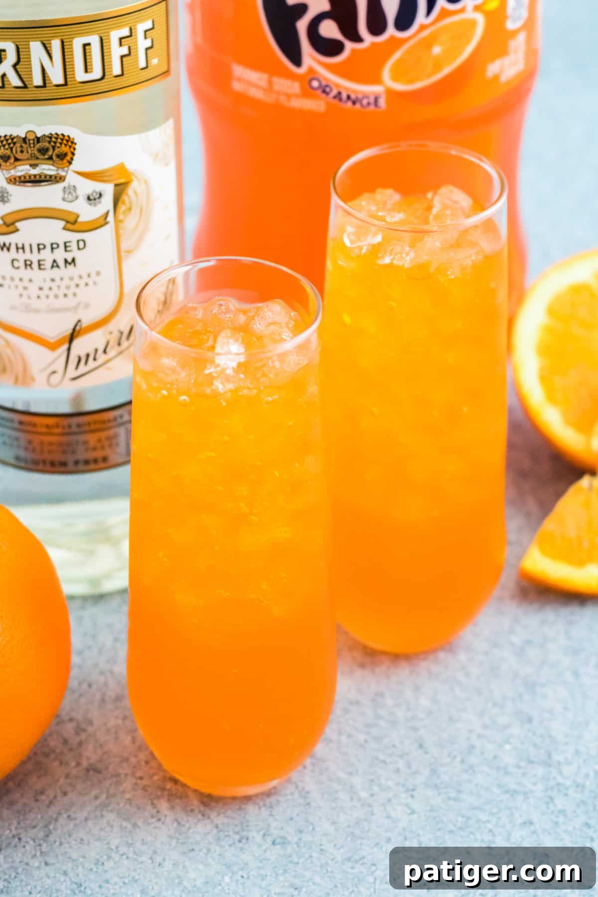 A vibrant orange cocktail with vodka, half-filled in a glass with ice. The drink has a bubbly texture, indicating the addition of soda, and is ready for its final touches.