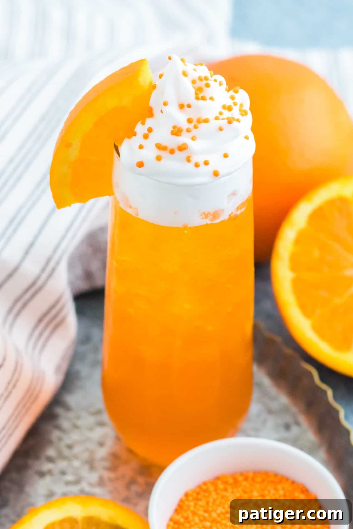 A close-up shot of a creamsicle drink recipe, showcasing the vibrant orange cocktail with a generous swirl of whipped cream on top, garnished with a fresh orange wedge. The texture is inviting and refreshing.