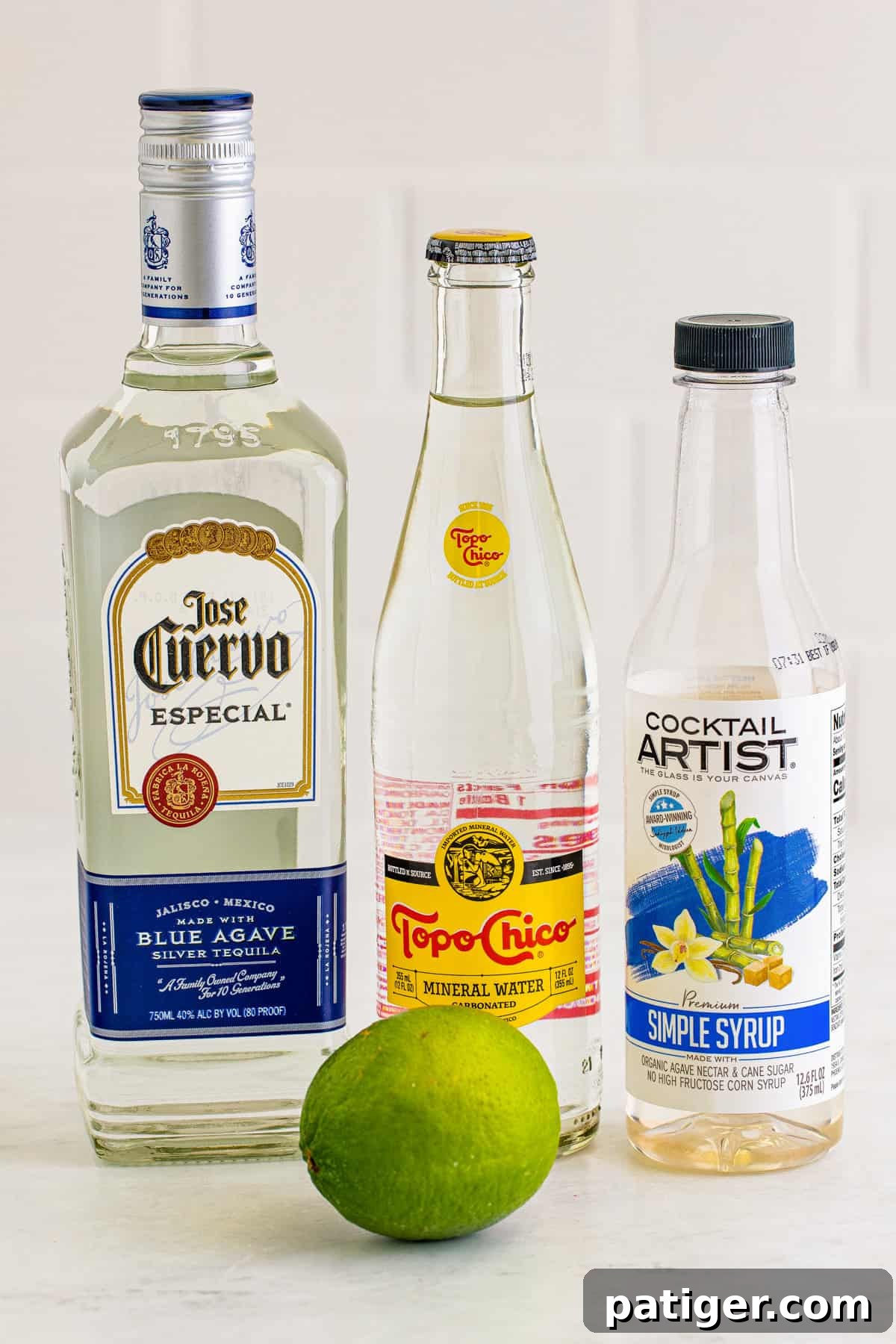 Ingredients for a Ranch Water cocktail: a bottle of blanco tequila, Topo Chico mineral water, a bottle of simple syrup, and fresh limes.