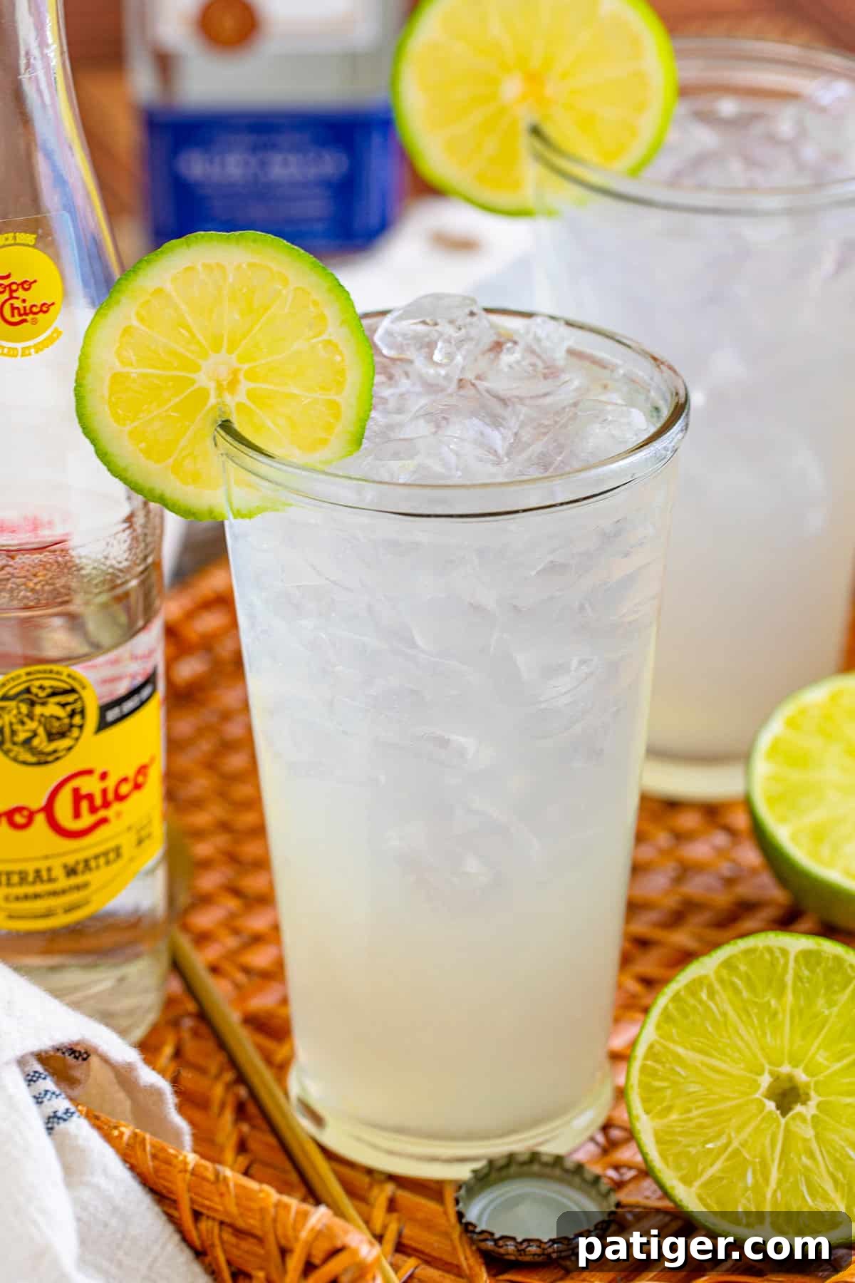 A glass of Ranch Water cocktail with tequila, fresh lime, and Topo Chico, garnished with a lime wedge, sitting on a straw tray.