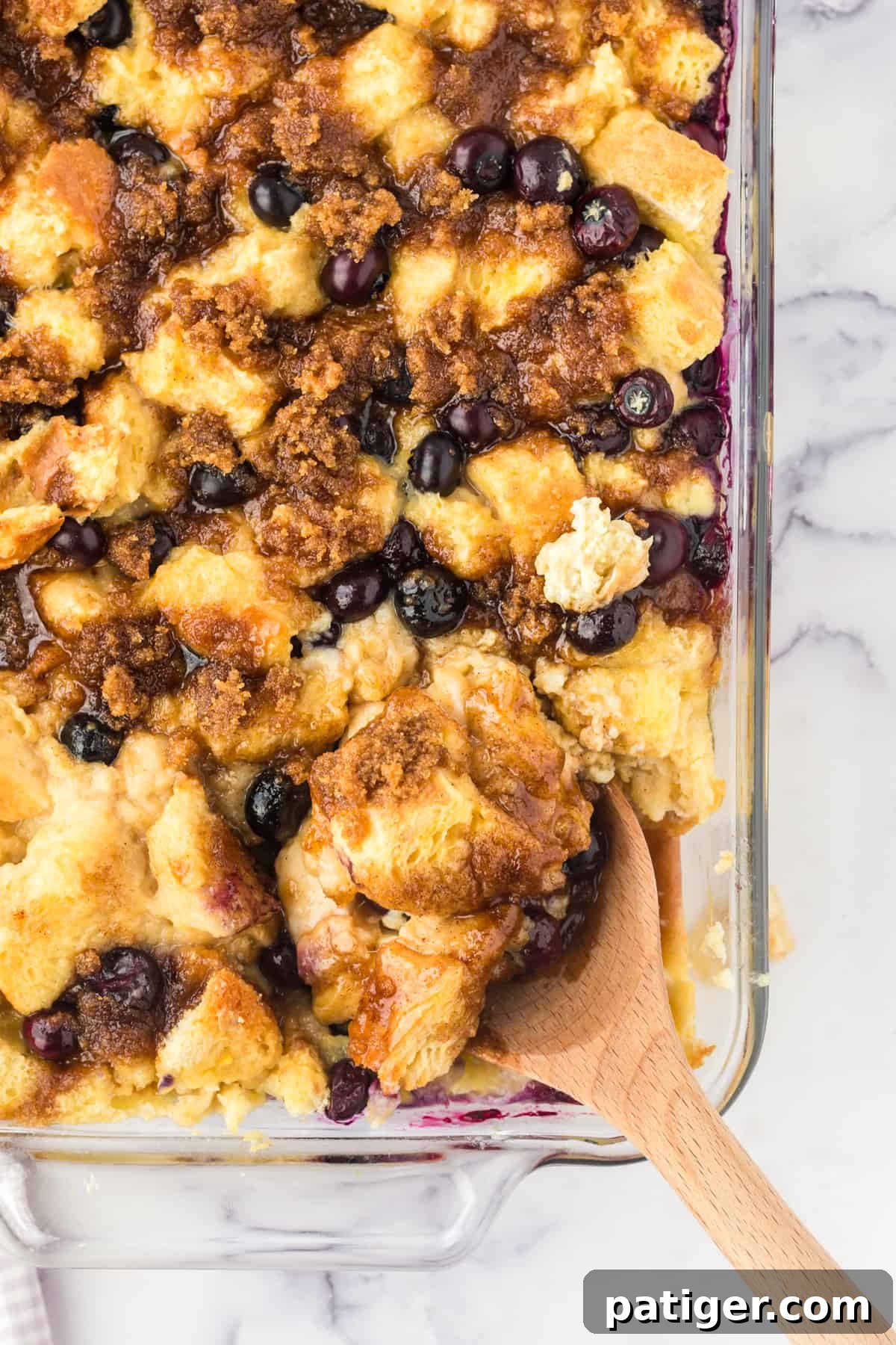 A serving of blueberry French toast casserole being scooped from a baking dish, showcasing the golden-brown crust and juicy blueberries.