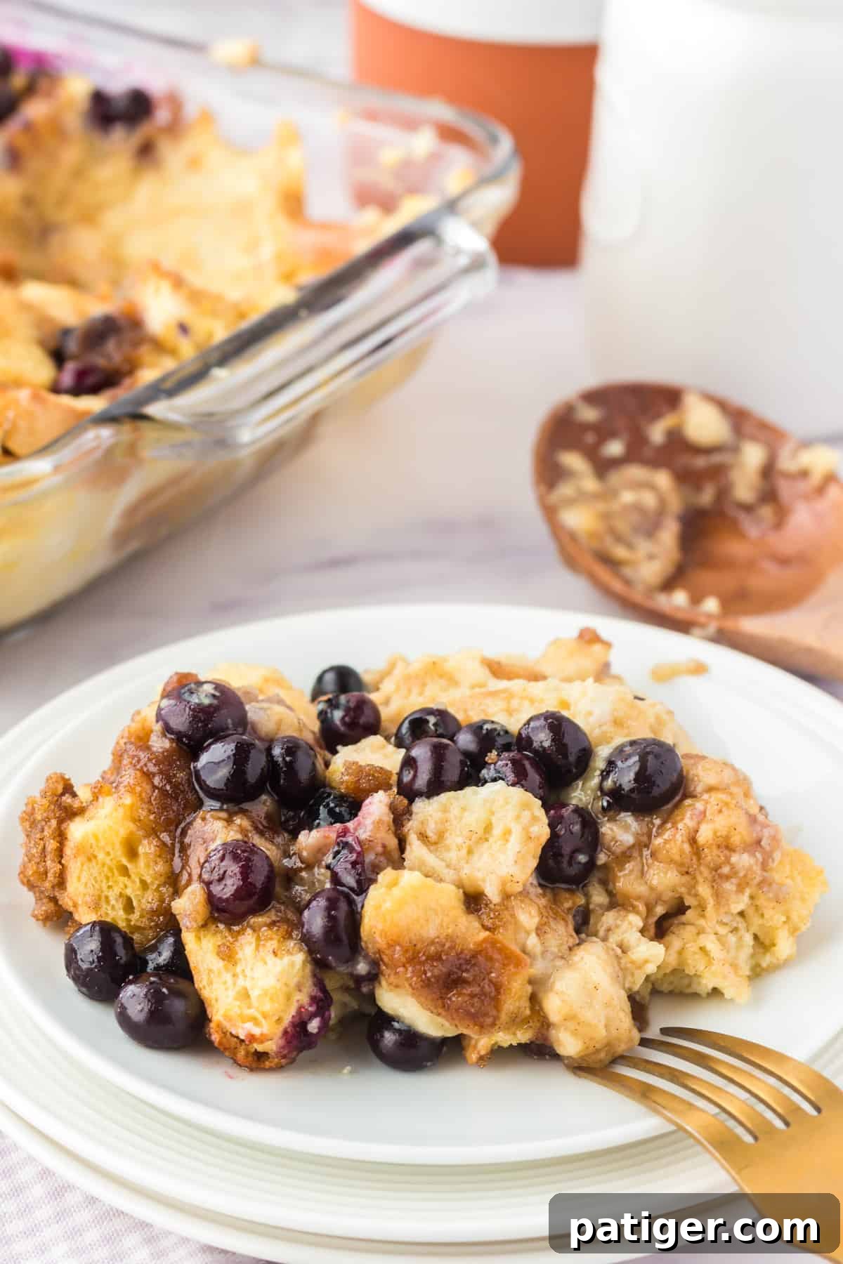 A slice of blueberry overnight French toast casserole on a white plate, with the full baking dish in the background, ready to be served.