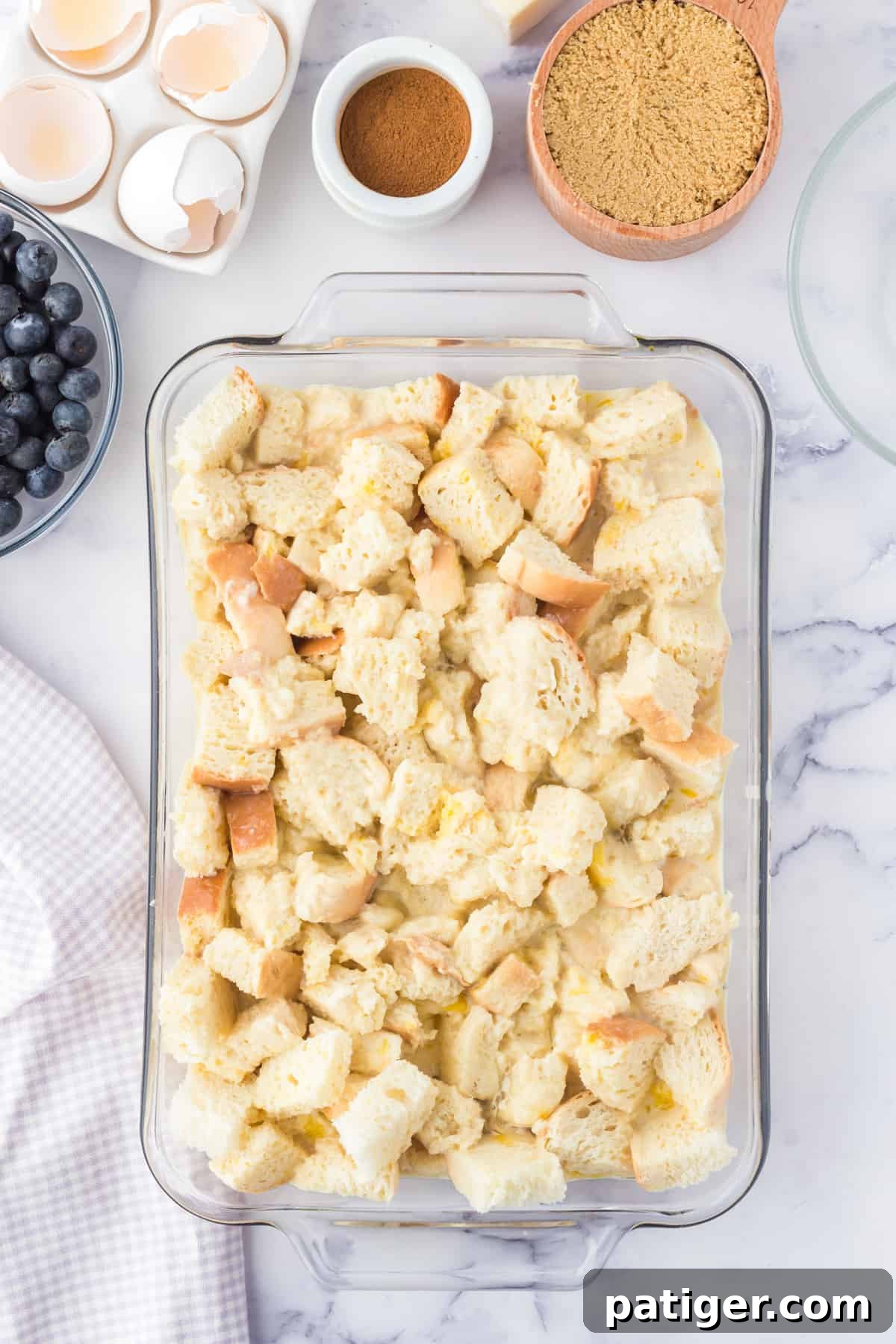 A casserole dish filled with cubed bread soaking in the egg custard mixture for blueberry French toast casserole.