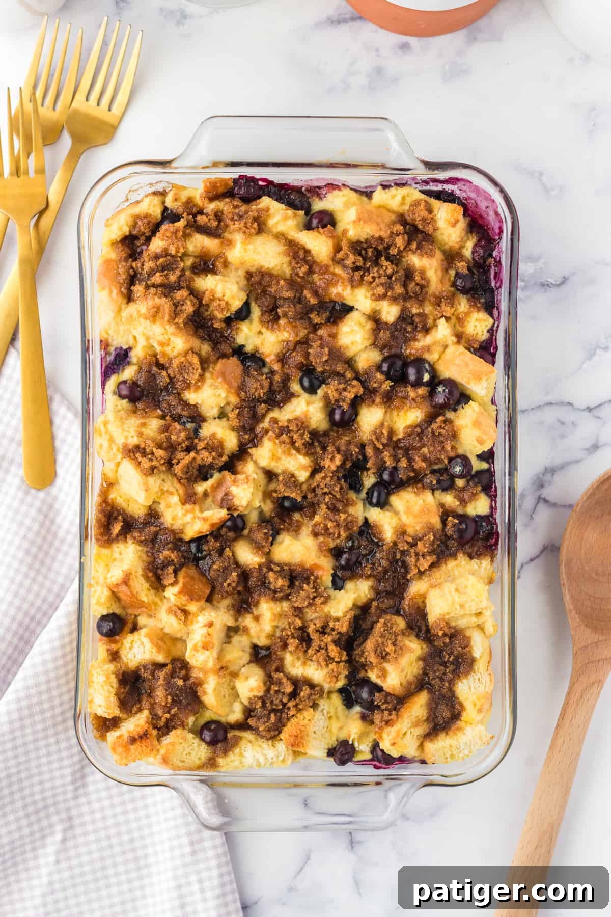 A freshly baked, golden brown blueberry French toast casserole in a baking dish, with a serving spoon and forks nearby.
