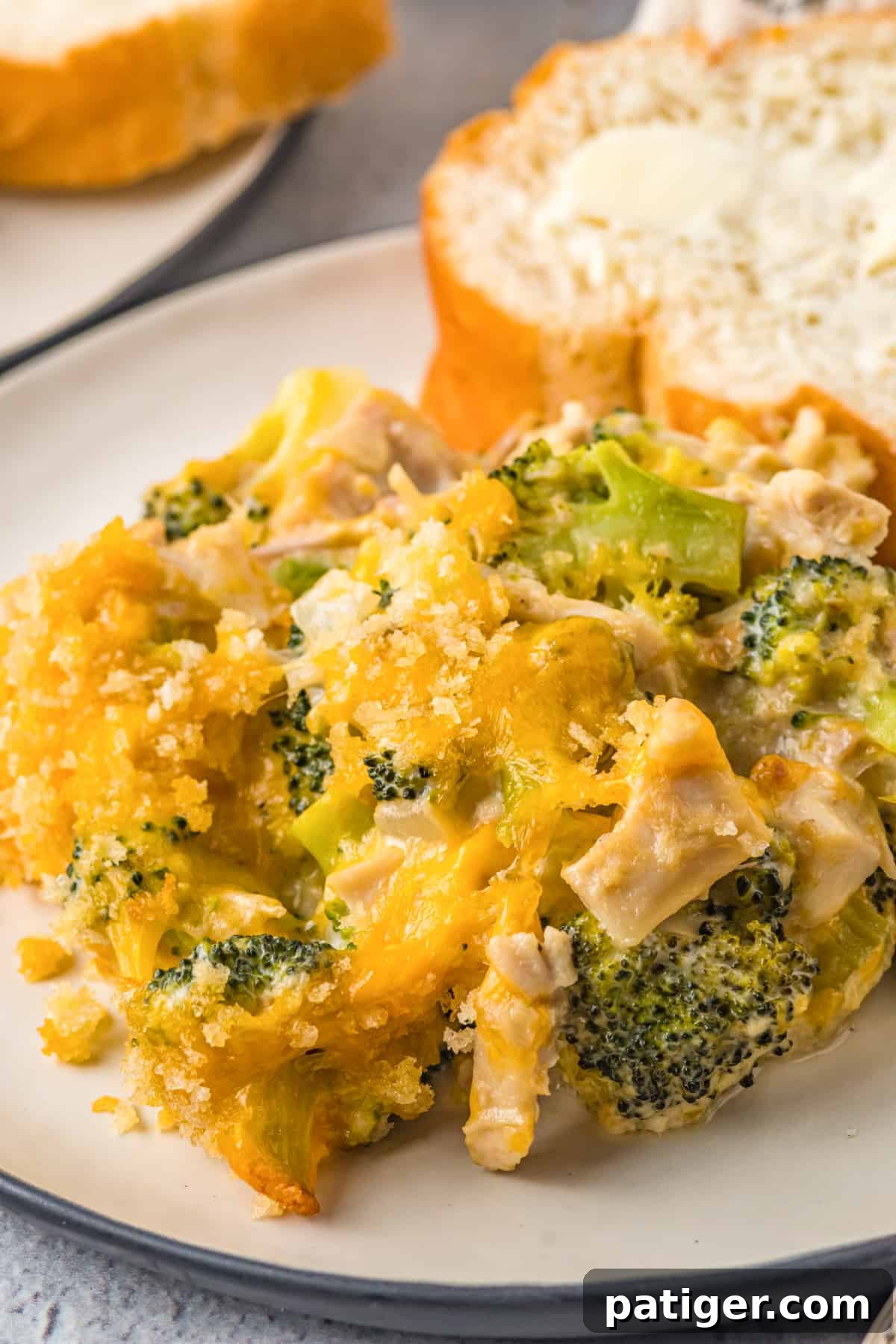 Creamy chicken and broccoli casserole on a white plate with piece of bread.