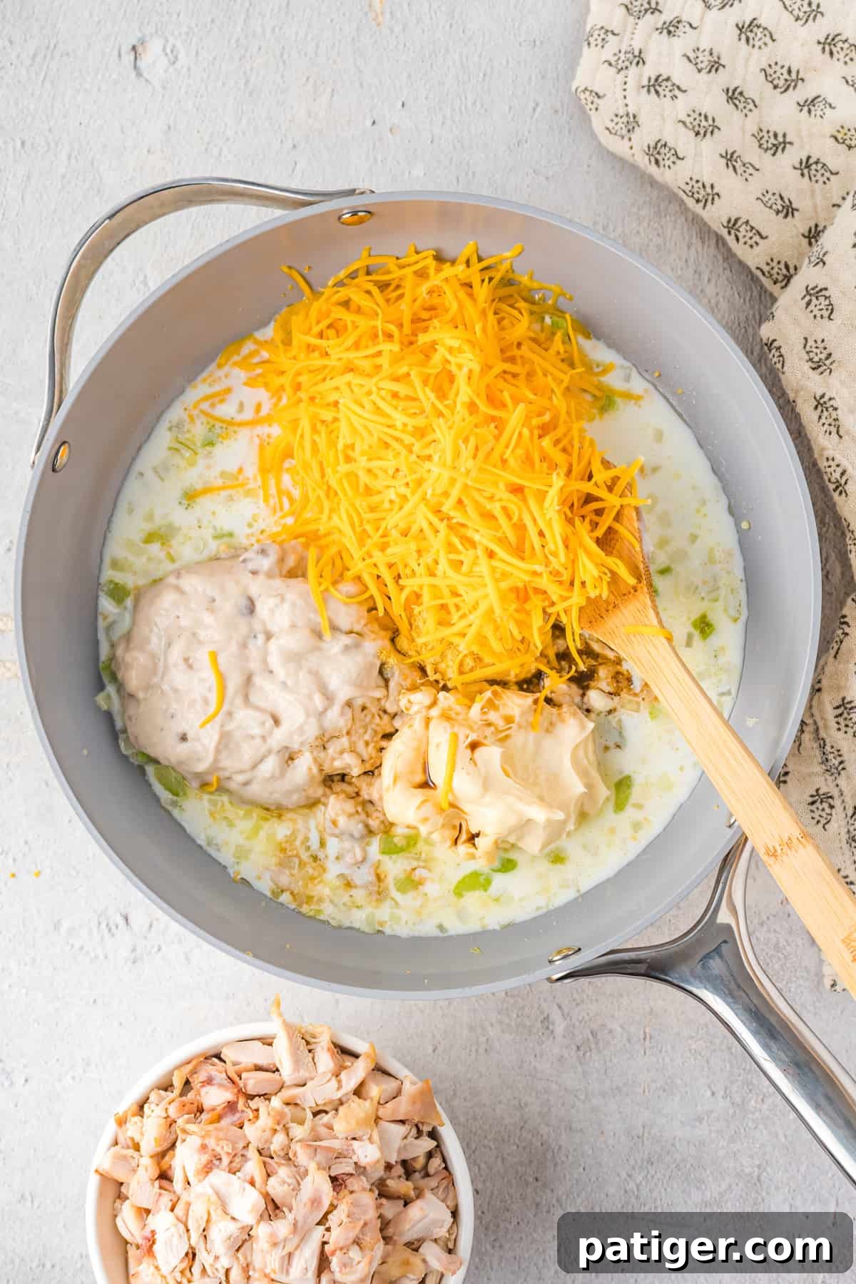 Shredded cheese, soup, mayo, sour cream, and other ingredients added to pan.