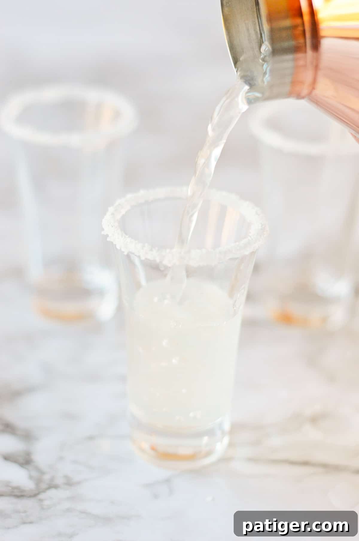 Cocktail shaker pouring lemon drop into rimmed shot glass.