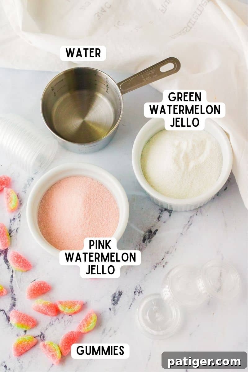 A flat lay photograph showcasing the ingredients for watermelon vodka jello shots, including boxes of green and pink gelatin mixes, a glass of water, and a pile of sour watermelon gummie candies.