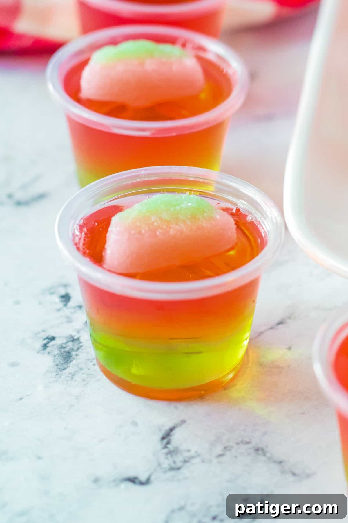A single pink and green layered watermelon jello shot, perfectly set and topped with a sour watermelon candy, ready to be enjoyed.