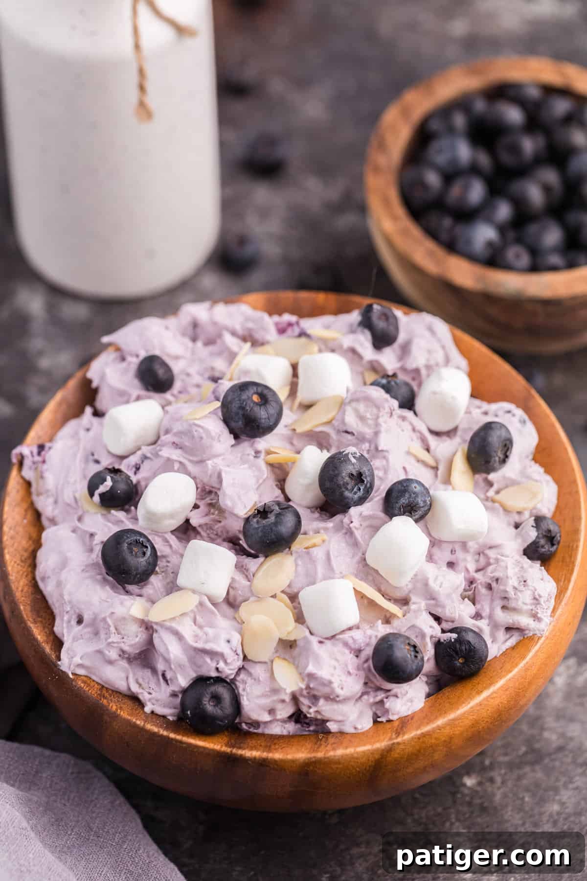 Whipped Blueberry Bliss 2 Blueberry fluff salad in a wooden bowl, topped with mini marshmallows, fresh blueberries, and almond slivers, ready to be served.