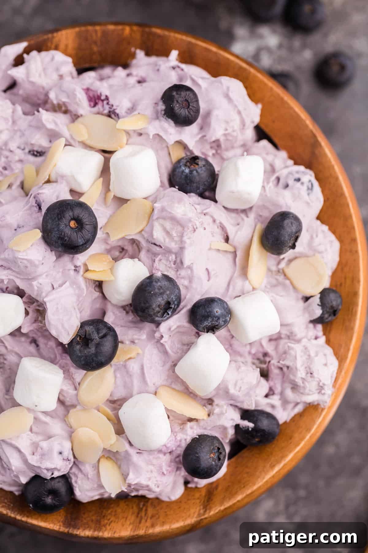 Whipped Blueberry Bliss 3 Light and creamy blueberry fluff dessert salad topped with fresh blueberries, mini marshmallows, and sliced almonds, presented in a clear glass bowl.