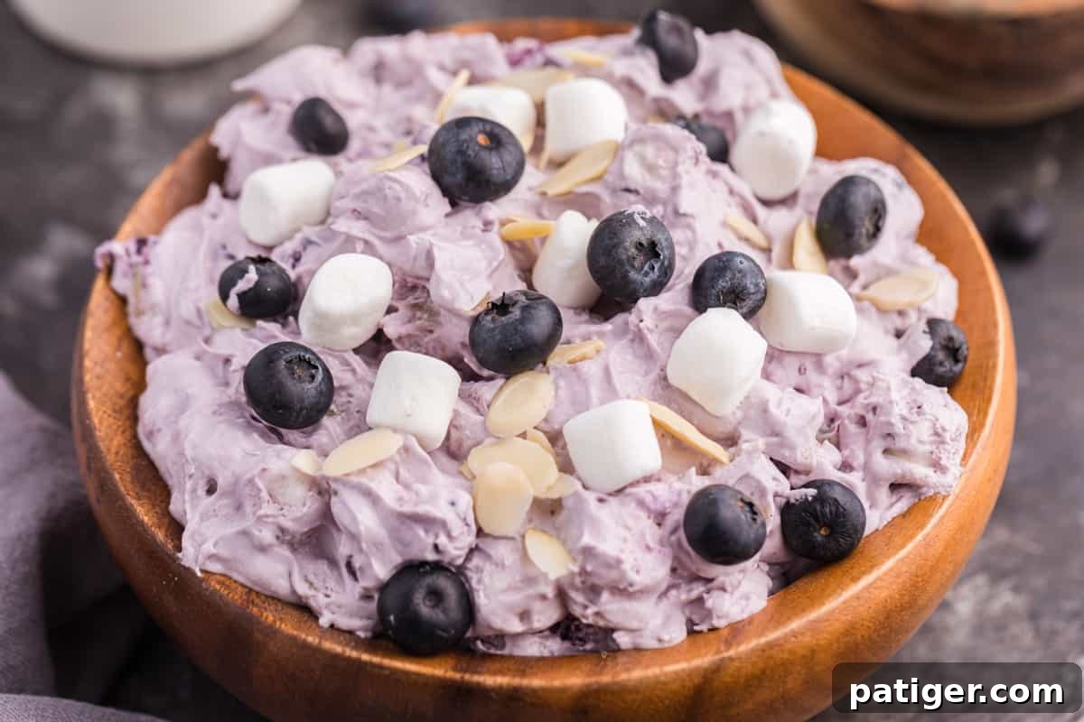 Whipped Blueberry Bliss 7 Blueberry fluff dessert salad served in a decorative wooden bowl, garnished with fresh blueberries, mini marshmallows, and almond slivers.