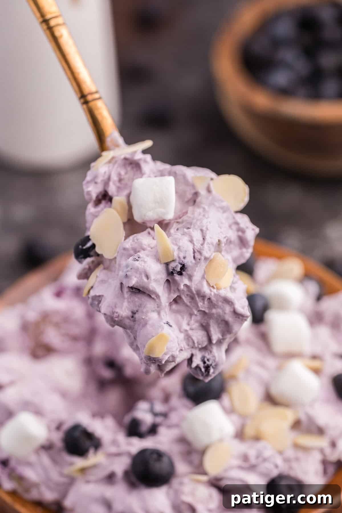 Whipped Blueberry Bliss 8 A spoonful of fluffy blueberry salad being lifted out of a rustic wooden bowl, showcasing its creamy texture and fruit pieces.