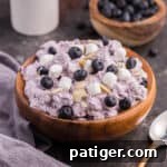 Blueberry fluff salad in a wooden bowl, topped with mini marshmallows, fresh blueberries, and almond slivers, ready to be served.