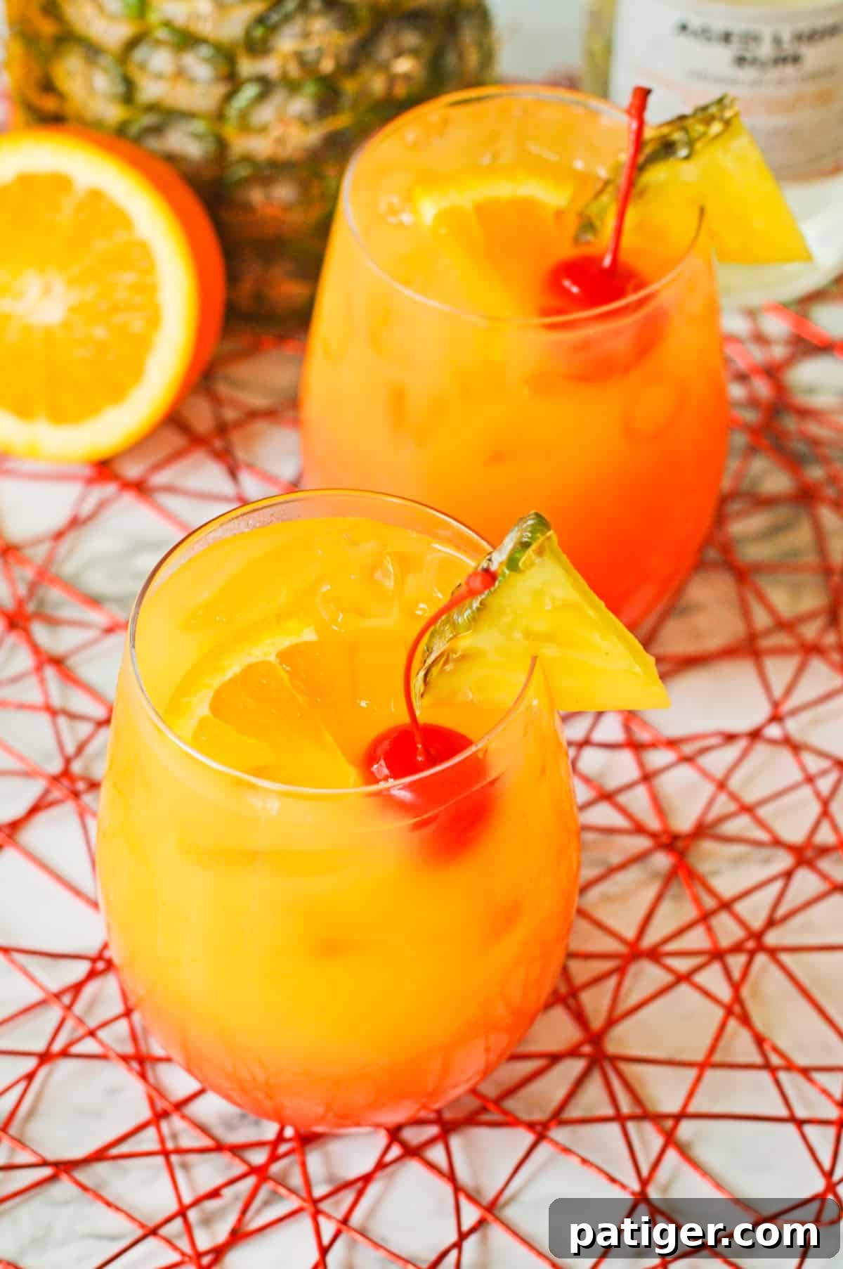 Two Rum Punch cocktails garnished with fresh pineapple wedges, cherries, and orange slices, perfect for a tropical gathering.