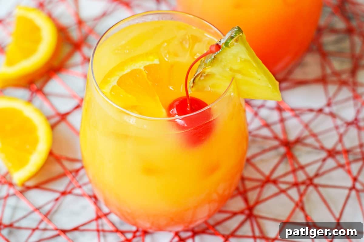 A beautifully layered yellow, orange, and red ombre cocktail garnished with a maraschino cherry, orange slice, and pineapple wedge, showcasing a perfect Caribbean Rum Punch.