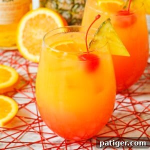 Yellow, orange, and red Caribbean Rum Punch cocktail garnished with cherry, pineapple, and oranges.