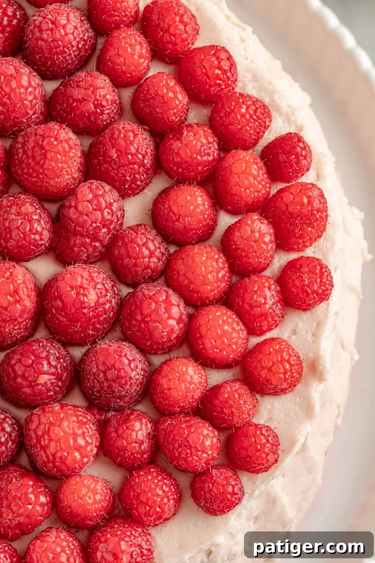 A beautifully round cake topped with pink frosting and an abundance of fresh raspberries.