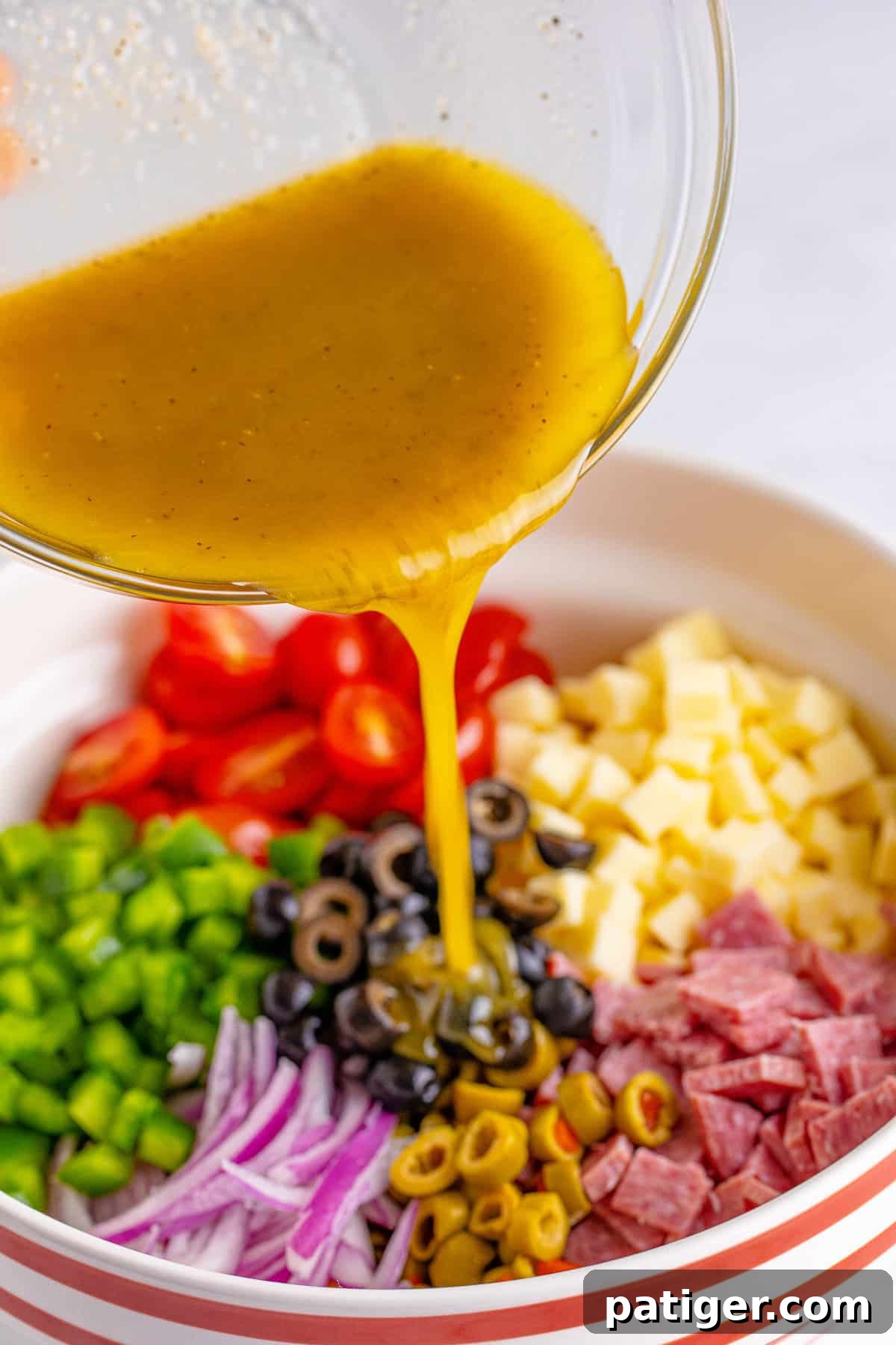 Homemade Italian dressing being poured over the colorful pasta salad ingredients in a large mixing bowl, illustrating Step 3 of the recipe.