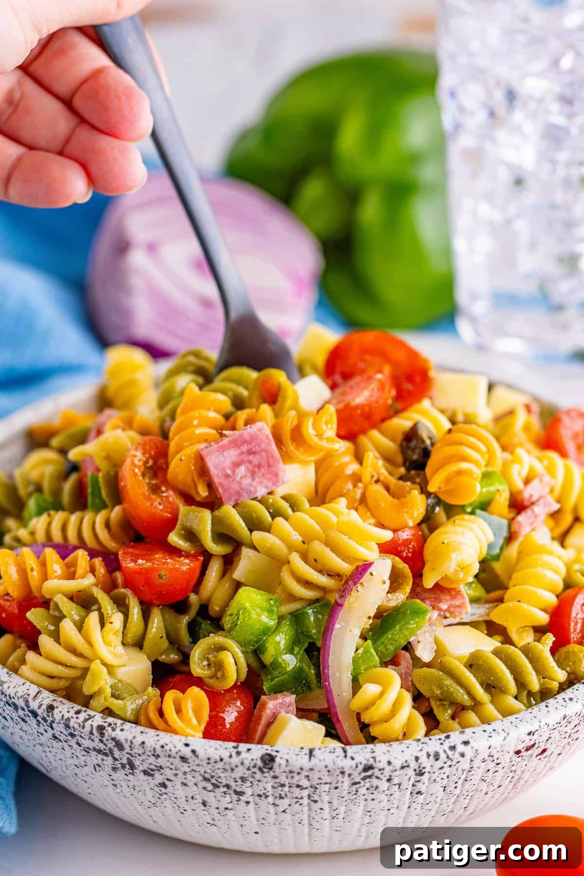 Hand reaching with a fork into a large bowl of Tri-Color Rotini Pasta Salad, ready to enjoy