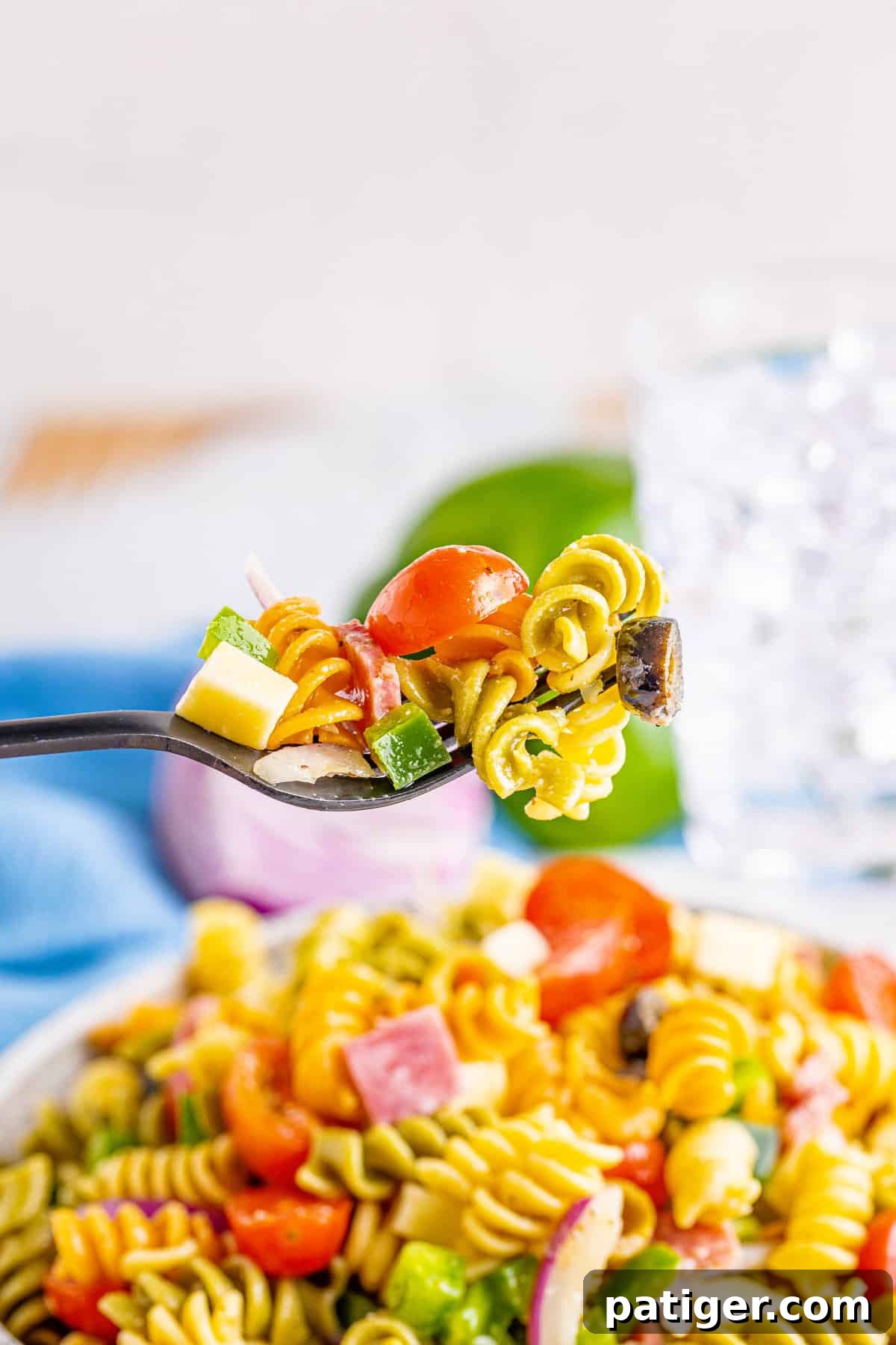 Fork with a perfect bite of Tri-Color Pasta Salad, featuring rotini, grape tomato, green bell pepper, and mozzarella cheese