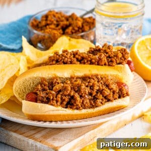 Hot dogs topped with homemade chili sauce on a plate with potato chips.