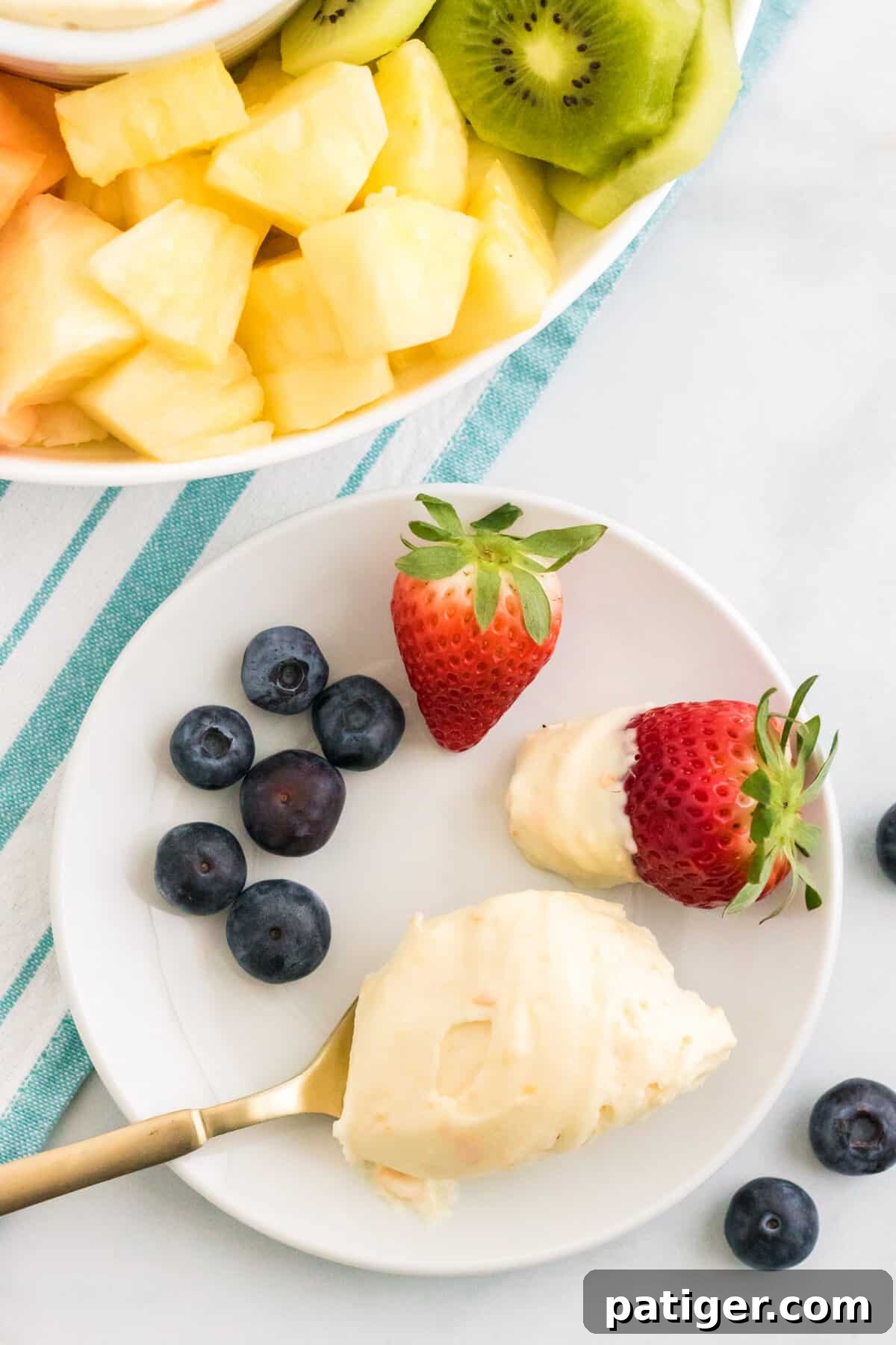 Spoonful of creamsicle fruit dip on a white plate with fresh fruit.