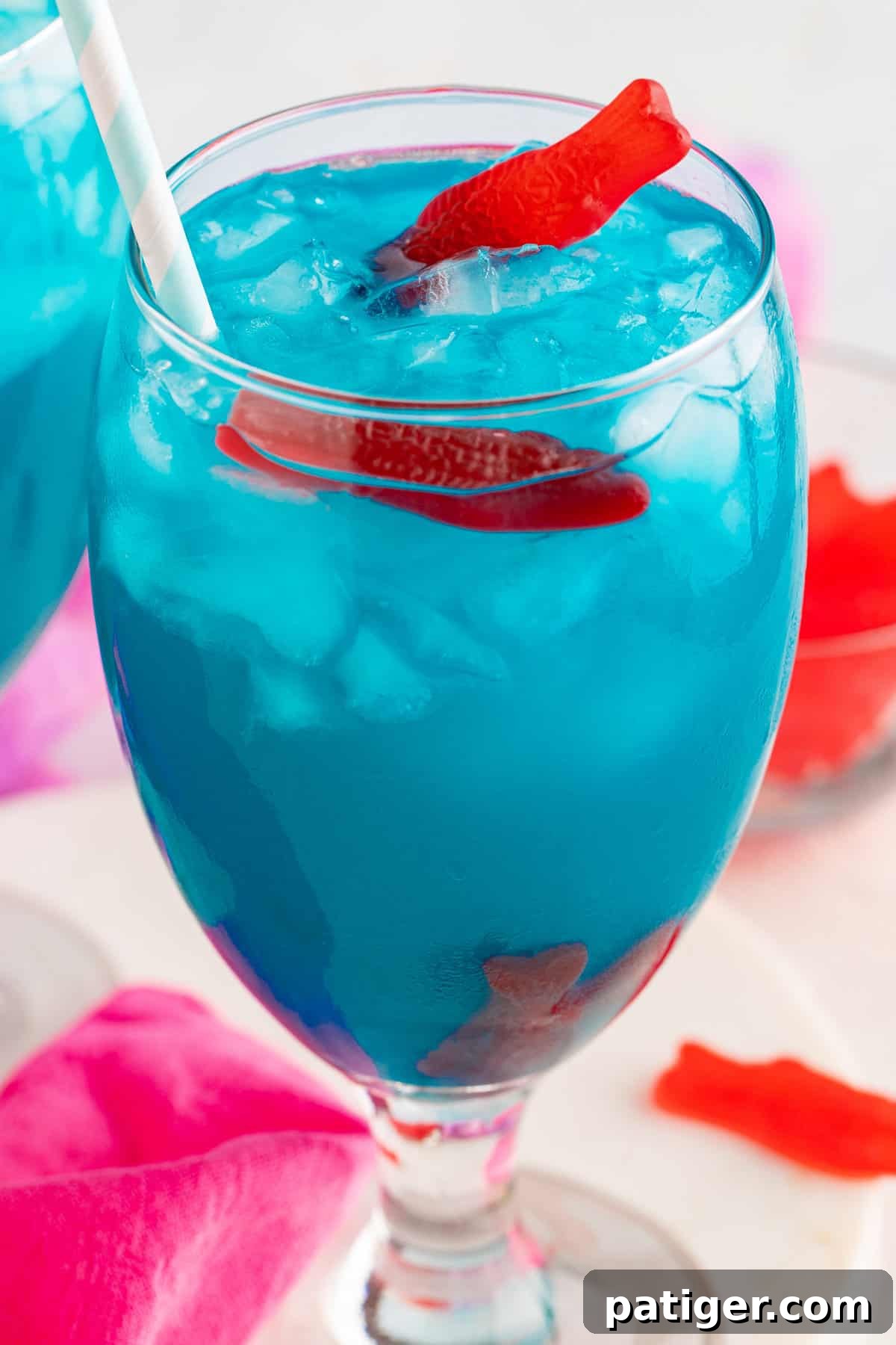 Blue ocean water cocktail in a wine glass with red candy fish sticking out of the top.