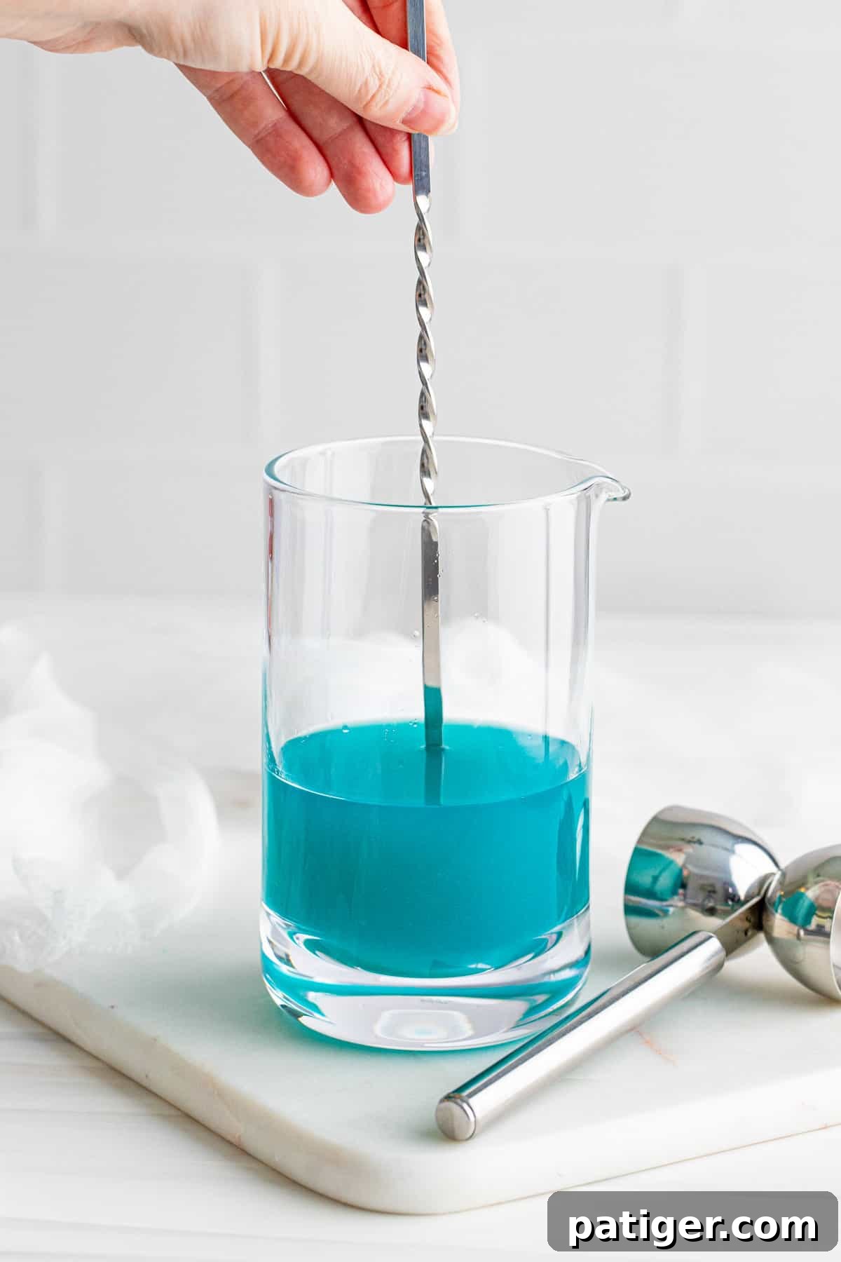 Stirring blue cocktail in large mixing glass.