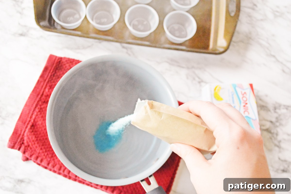 Blue ocean water jello mix being stirred with boiling water in a small saucepan on a stovetop.