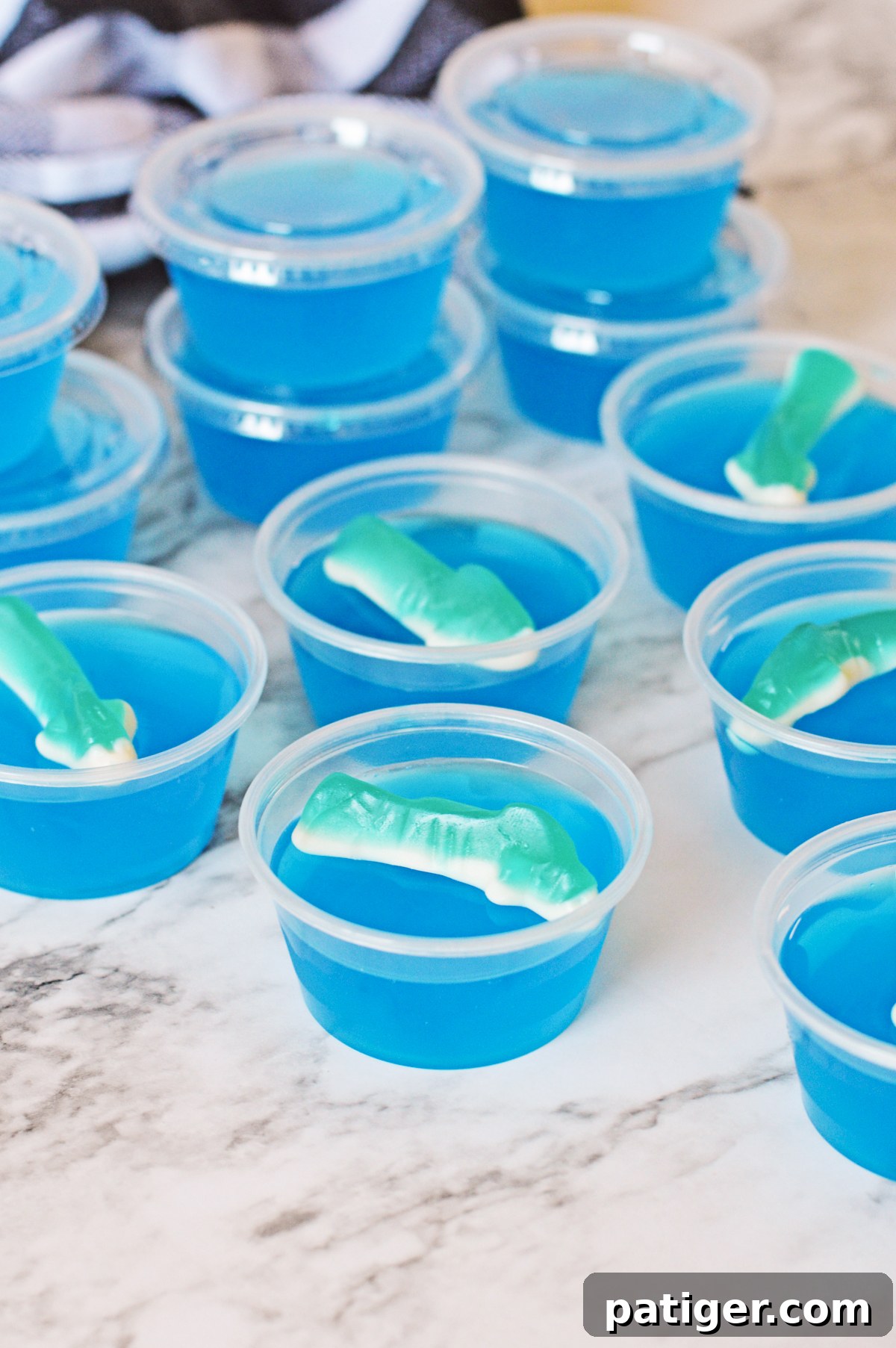 Shark bite jello shots topped with shark gummies, some with lids on the shot cups, ready to be served.