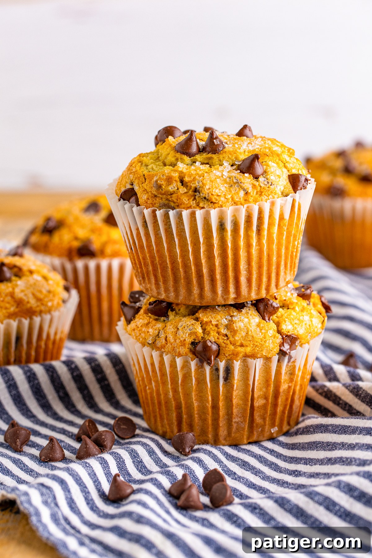 Ultimate Bakery Chocolate Chip Muffins 14 Two homemade chocolate chip muffins artfully stacked on top of one another, highlighting their height and texture.