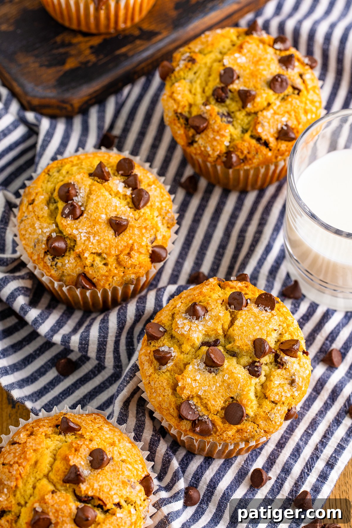 Ultimate Bakery Chocolate Chip Muffins 3 Top-down view of several jumbo chocolate chip muffins alongside a glass of milk, highlighting their generous size and golden tops.