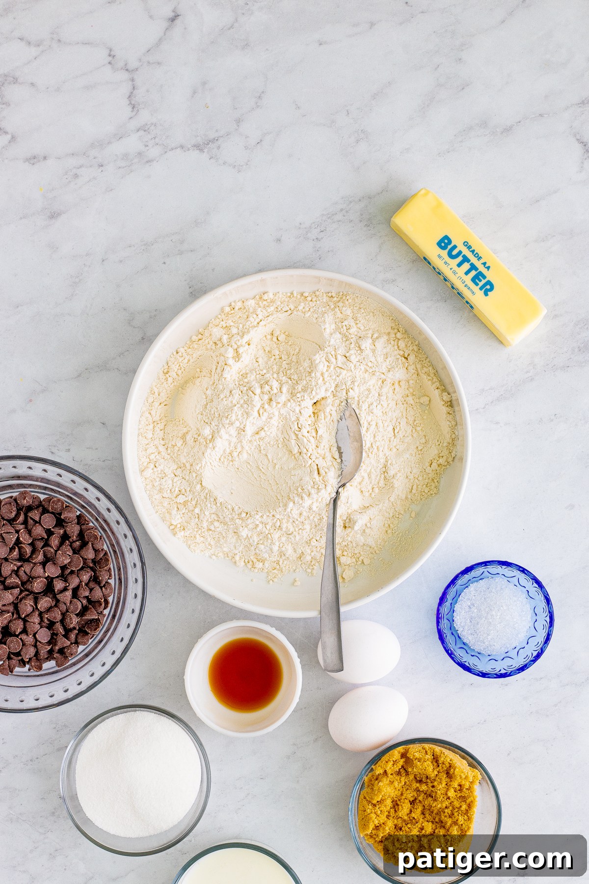 Ultimate Bakery Chocolate Chip Muffins 5 Dry ingredients for muffins, including flour, baking powder, and salt, in a mixing bowl with a spoon, surrounded by other ingredients.