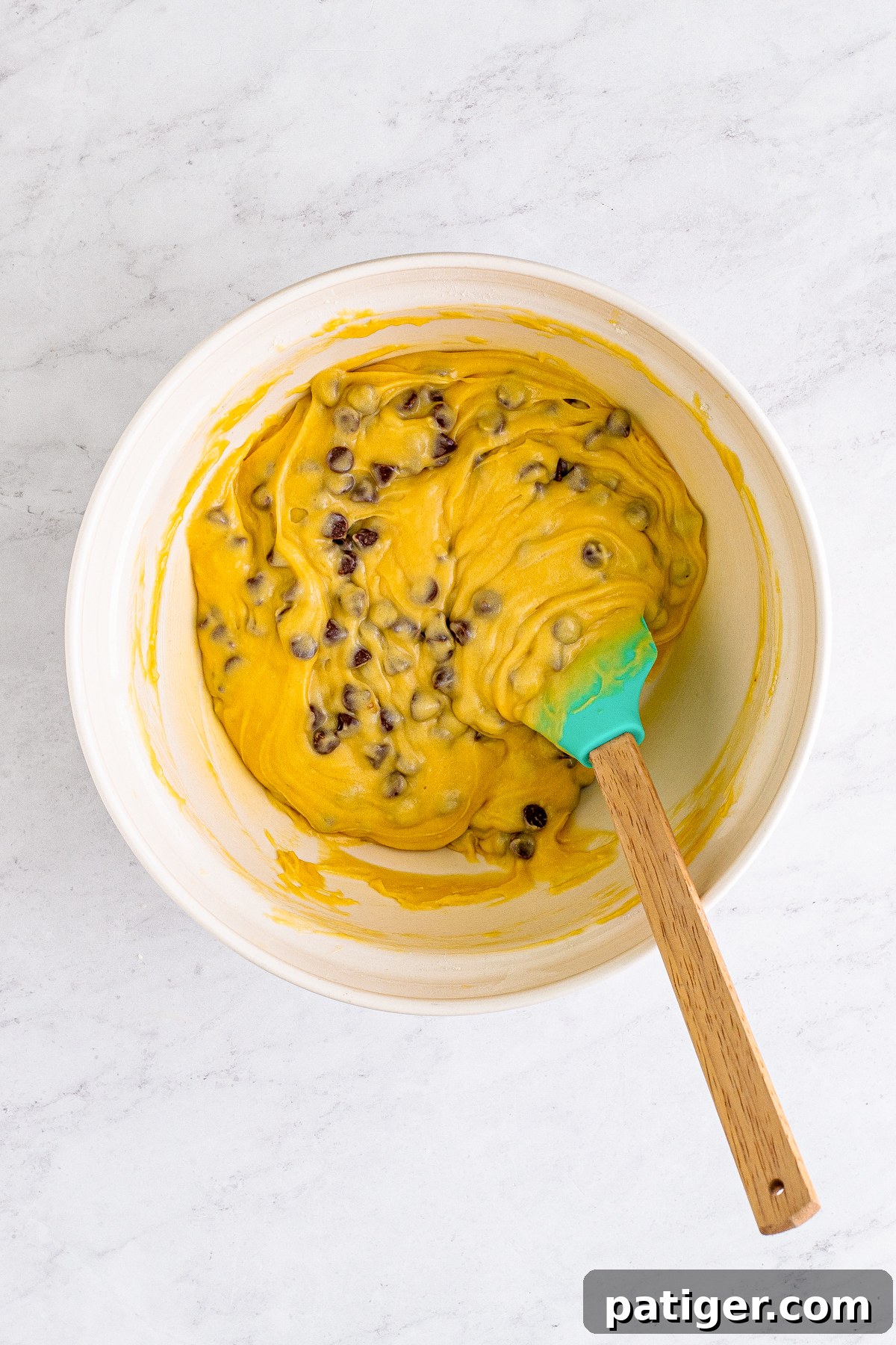 Ultimate Bakery Chocolate Chip Muffins 9 Chocolate chip muffin batter in a mixing bowl, ready for baking, with a spoon in the batter.