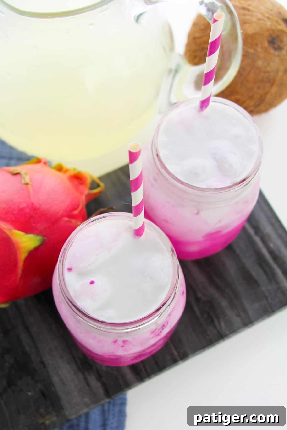 Two pink dragon drinks topped with coconut milk and whipped cream served in mason jars with pink and white striped paper straws.
