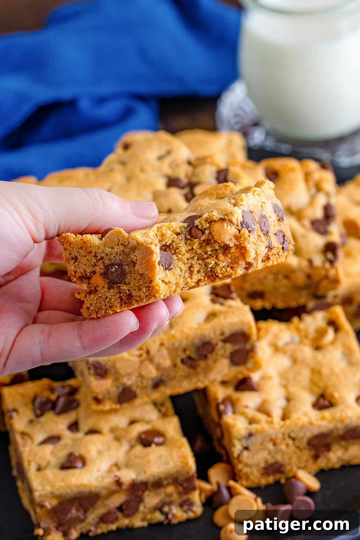 Peanut Butter Chocolate Chip Indulgence Bars 3 Hand holding cookie bar with bite taken out of it to show chocolate chip and peanut butter chip packed inside.