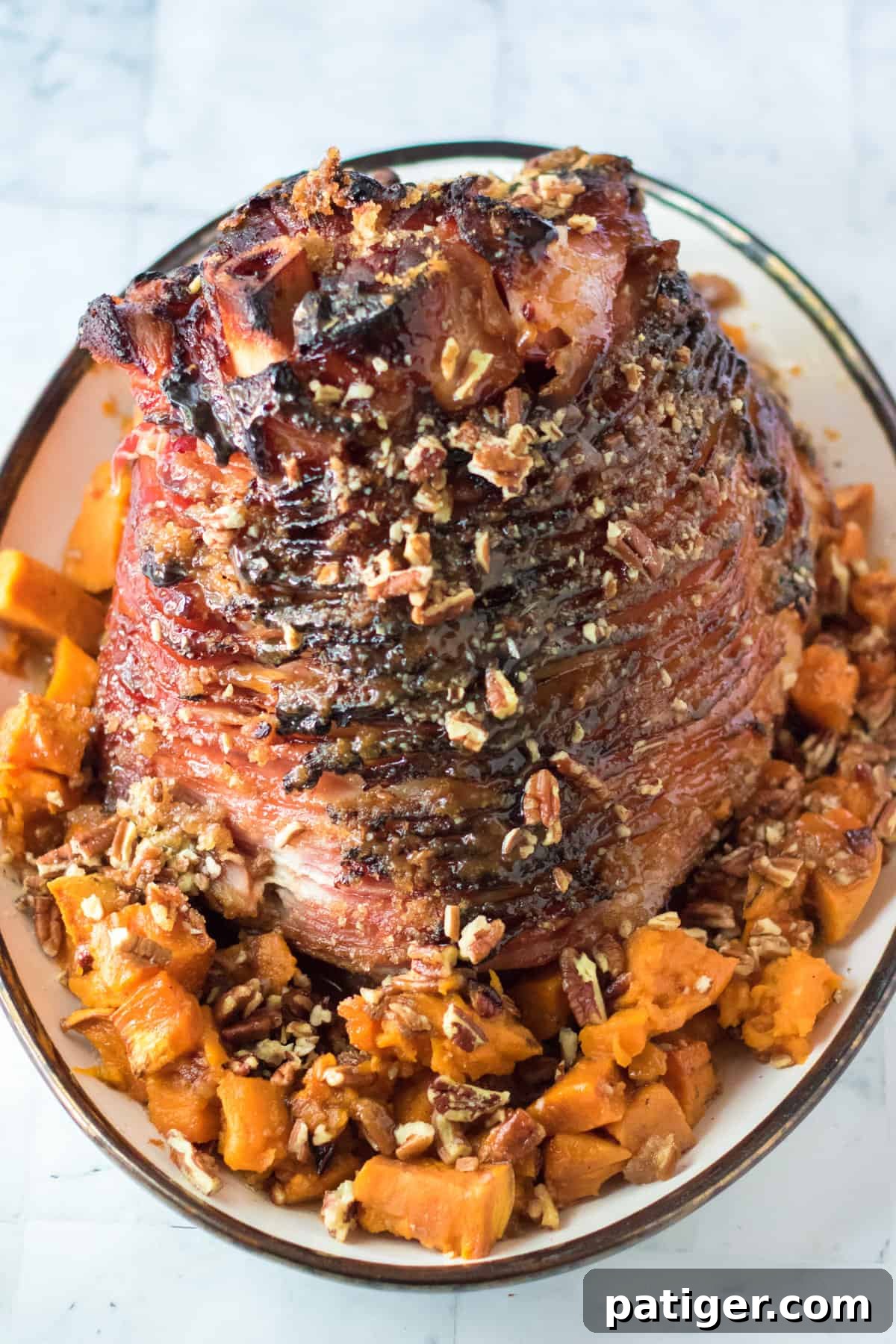 Maple pecan glazed bone-in ham served with pecan-topped sweet potatoes in a festive setting.