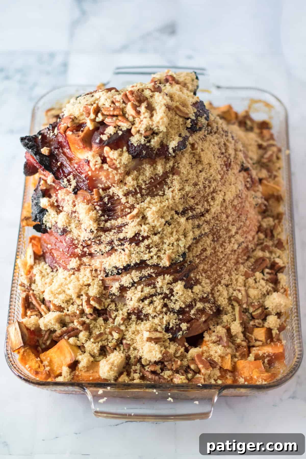 Spiral sliced ham in a baking dish, generously covered with brown sugar and pecans, halfway through baking.
