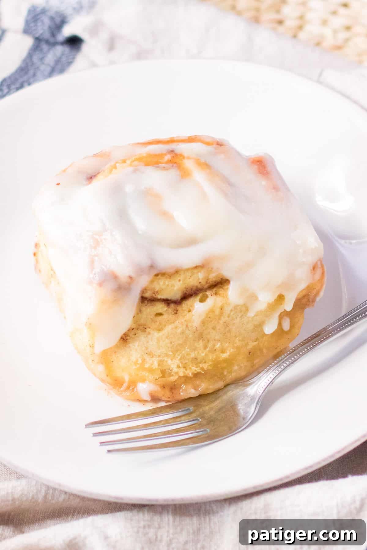 Large cinnamon roll with cream cheese icing on a white plate with a fork.