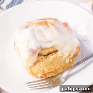 Large cinnamon roll with cream cheese icing on a white plate with a fork.