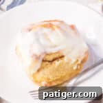 Large cinnamon roll with cream cheese icing on a white plate with a fork.