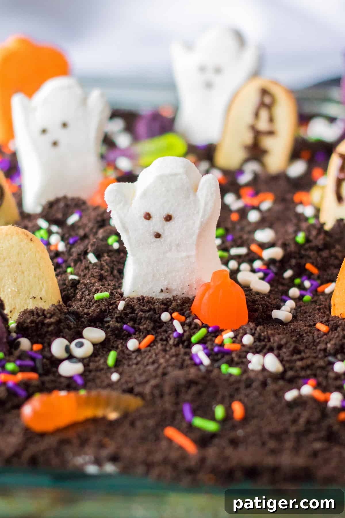 Haunted Cemetery Poke Cake 2 Ghosts in the graveyard halloween poke cake with marshmallow peep ghosts, pumpkins, cats, and cookie tombstones on top.