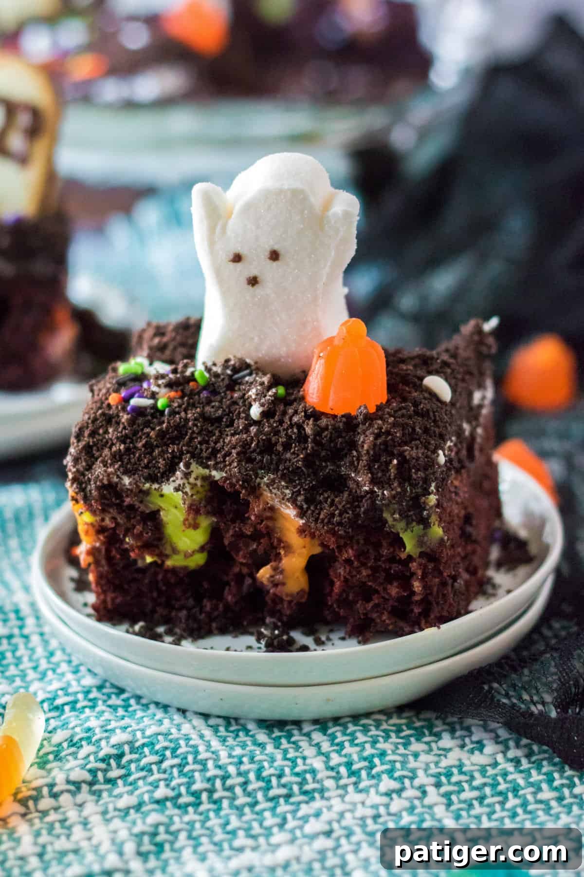 Haunted Cemetery Poke Cake 3 Piece of halloween poke cake with ghost and pumpkin candy on top.