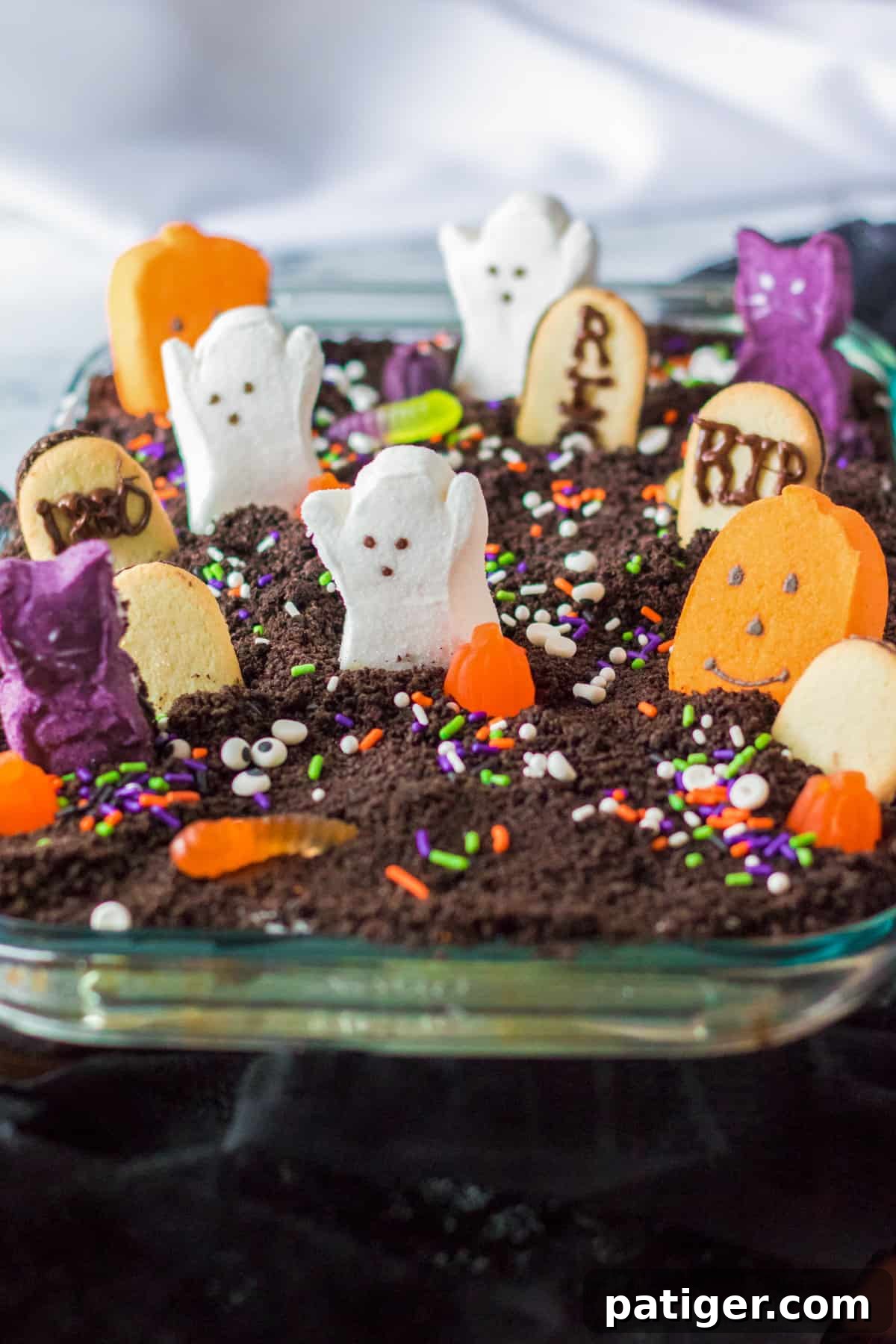 Haunted Cemetery Poke Cake 9 Ghosts in the Graveyard Dessert topped with peeps ghosts, cookie tombstonea, and other Halloween candy.
