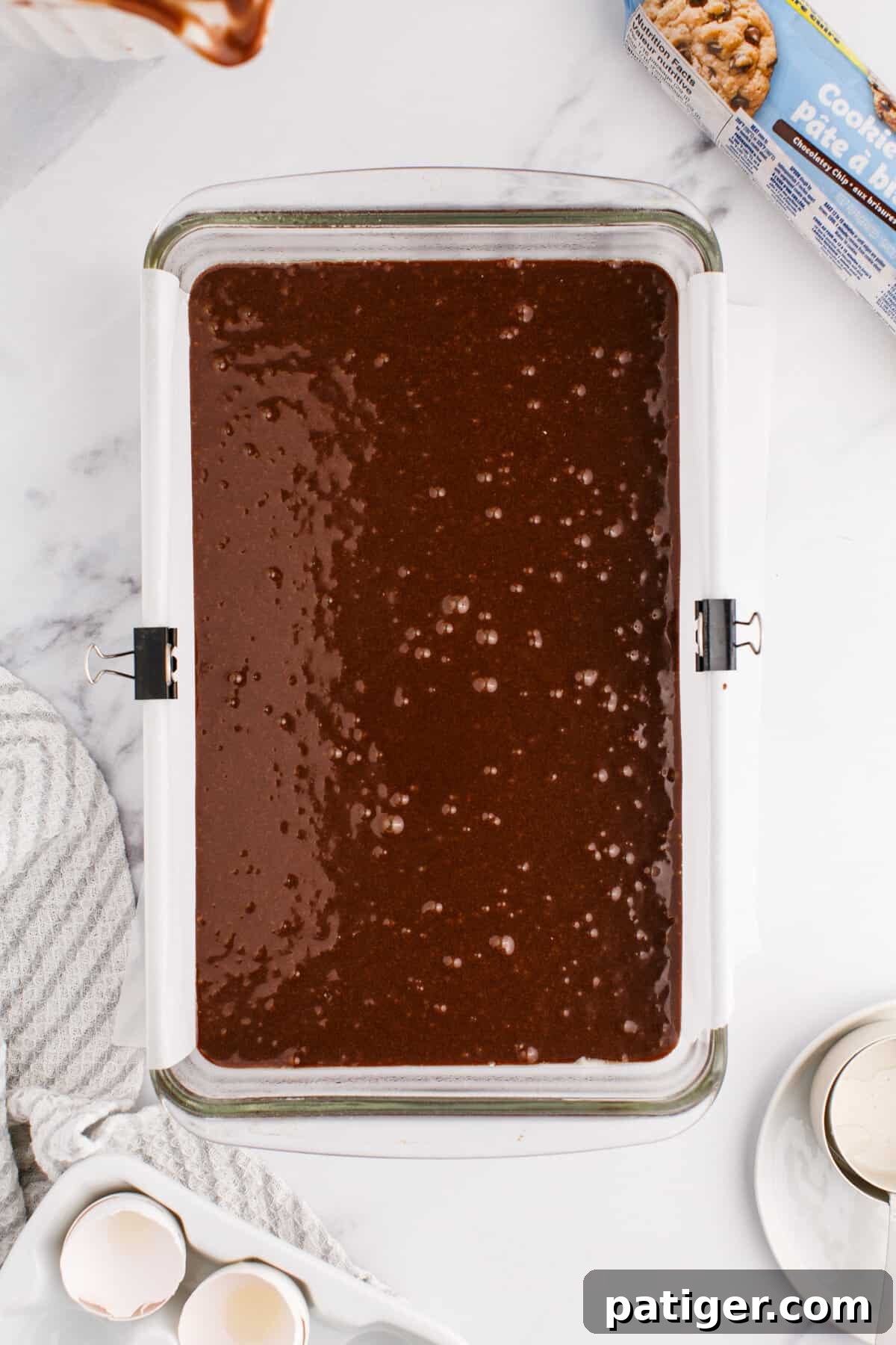 An even layer of rich brownie batter spread across the bottom of a baking pan, ready for the cookie dough.