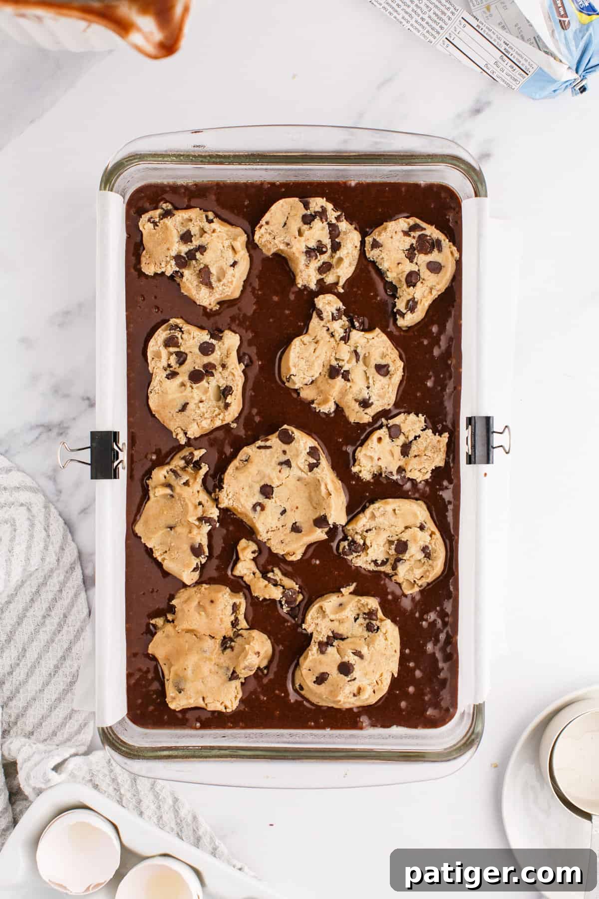 Chunks of chocolate chip cookie dough artfully placed on top of the brownie batter in a casserole dish, ready for baking.