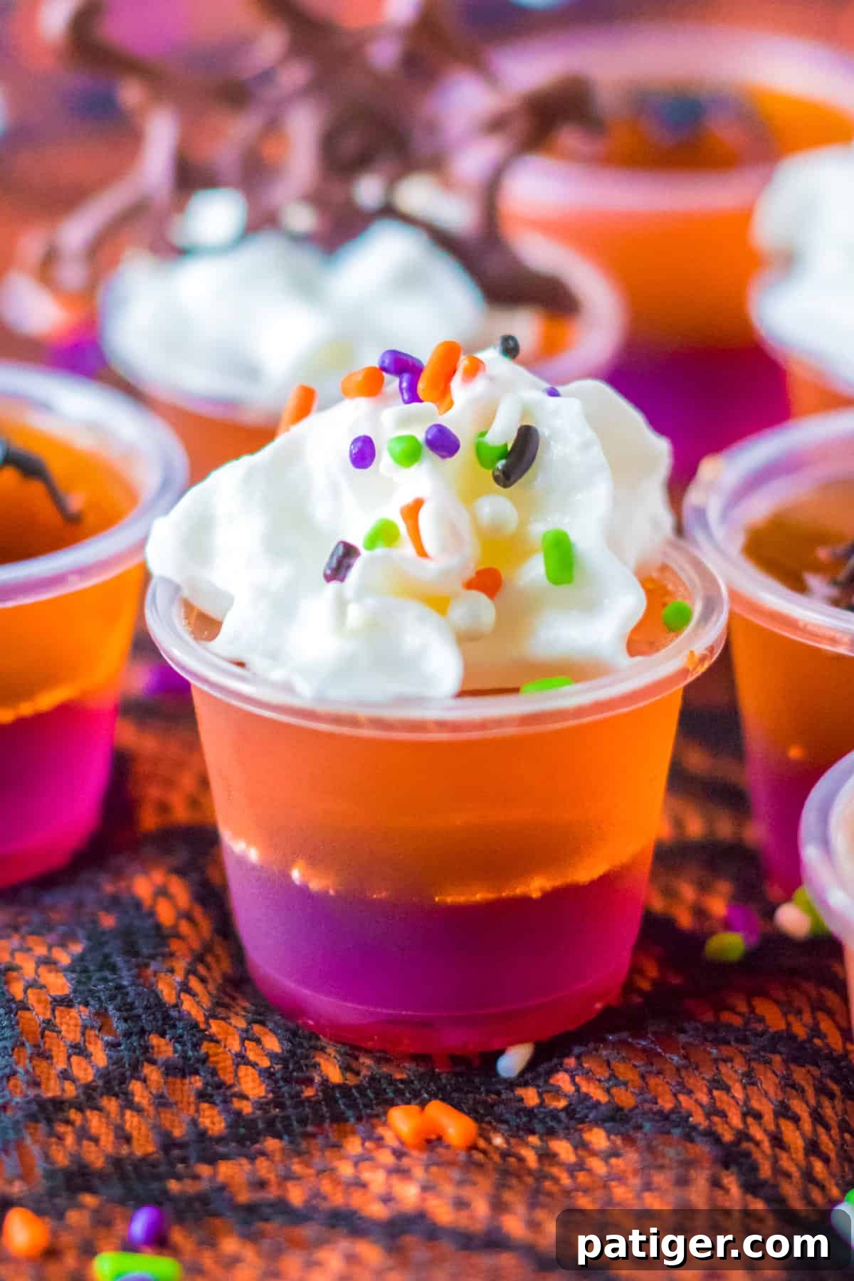 Purple and orange layered Halloween Jello Shots topped with whipped cream and sprinkles, ready for an adult Halloween party.
