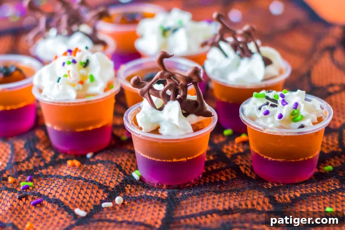 Halloween layered jello shots artfully decorated with whipped cream and delicate chocolate spider webs, enhancing their spooky appeal.